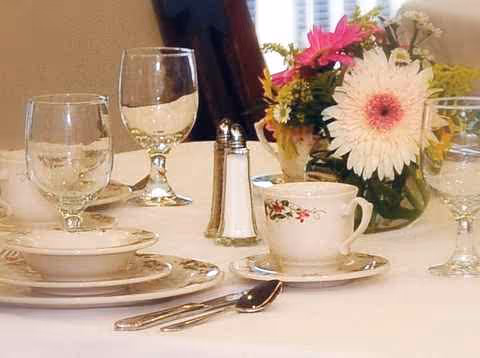 A dining table is set with china, glassware, silverware, and a floral centerpiece.