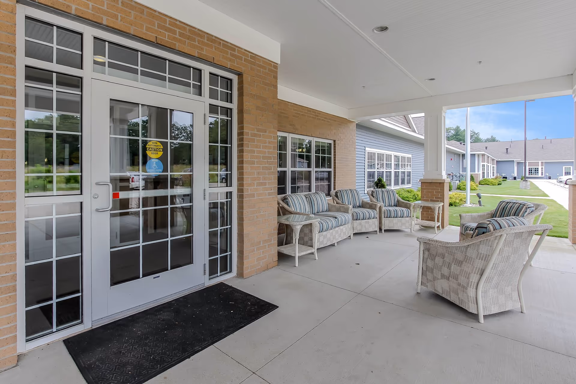 Covered front entrance patio with glass double doors and a seating area of wicker chairs and small tables.