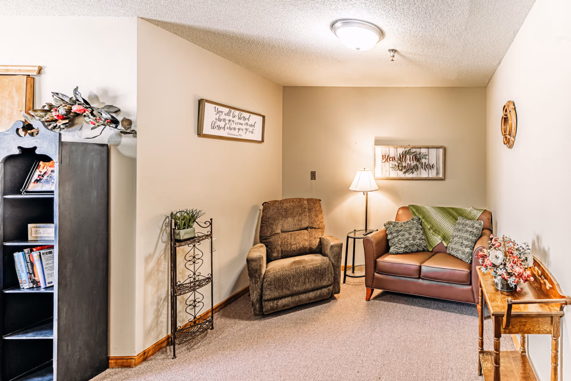 Cozy sitting area with a recliner and loveseat, a floor lamp, bookshelf, and decorative wall art.