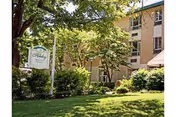 Exterior view of The Holiday Retirement Community - Skilled Nursing Home & Senior Rehabilitation building surrounded by green trees and bushes with a well-maintained lawn in front and a sign displaying the facility's name.