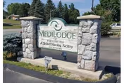 Stone sign at the entrance of Medilodge of Rochester Hills, a skilled nursing facility, with trees and a road in the background.