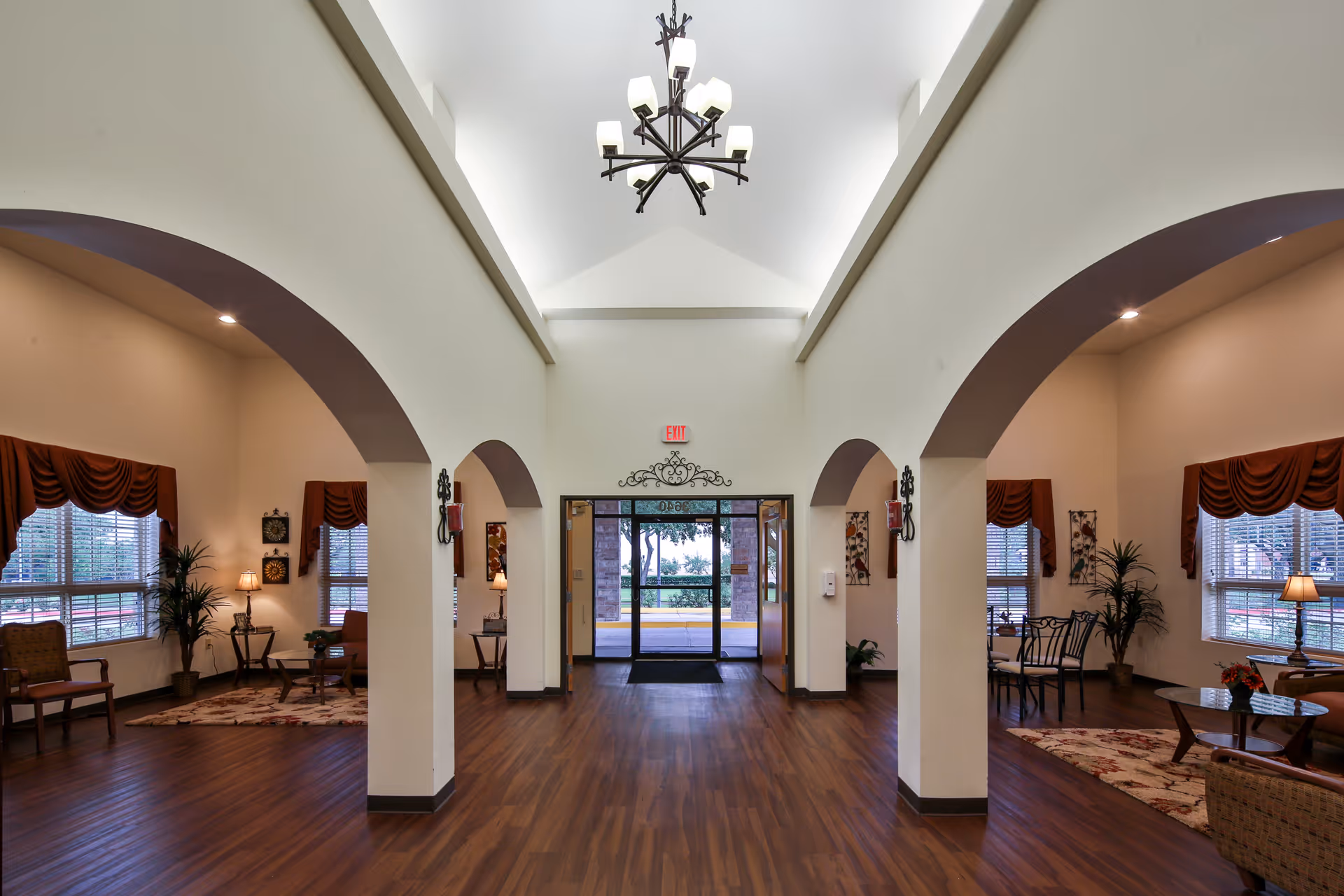 Spacious lobby interior with a vaulted ceiling and chandelier, arched columns, seating areas and glass entrance doors.