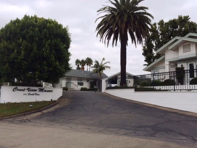 Entrance of Crestview Manor senior living with gate, sign, and palm trees.