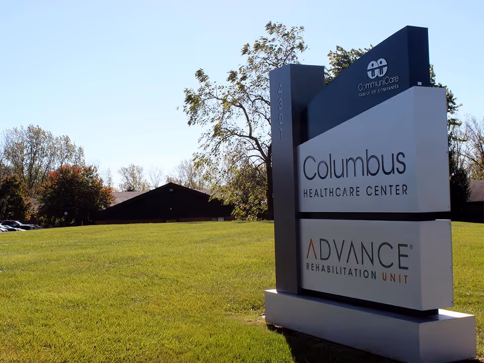 A freestanding sign for Columbus Healthcare Center and Advance Rehabilitation Unit on a grassy lawn with a building and trees in the background.