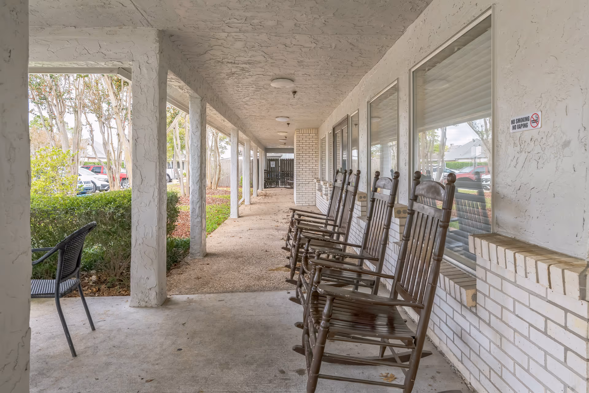 Covered front porch with a columned walkway lined with wooden rocking chairs outside the facility.