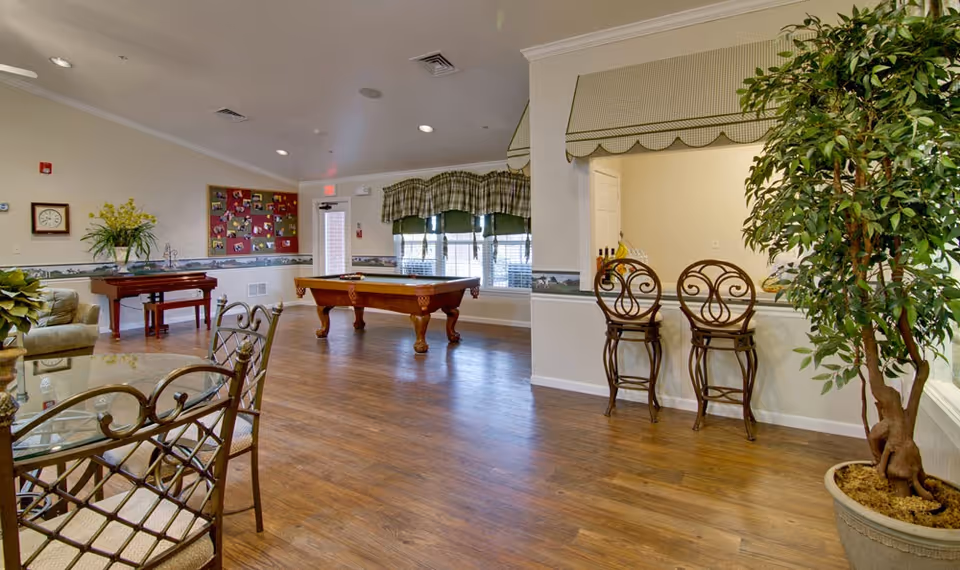 Community lounge with a pool table, seating area, bar stools, and potted plants on wood floors.