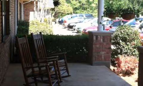 Covered patio with wooden rocking chairs and brick columns overlooking a parking lot.