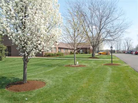 Exterior view of Pine Knoll facility with manicured lawn, trees, and parking.