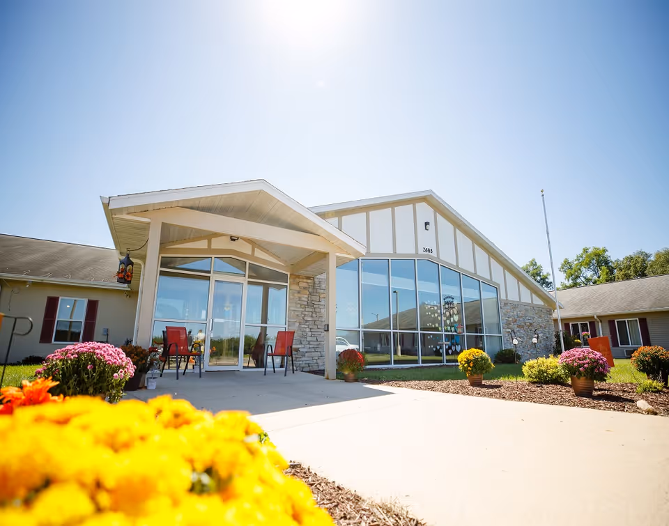 Front view of Heritage House of Portage Assisted Living with glass entrance and colorful flowers.
