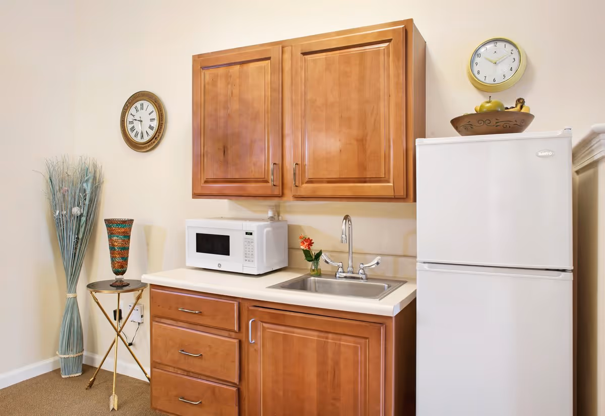 Compact kitchenette featuring wooden cabinets, a microwave on the counter, a sink, and a white refrigerator.