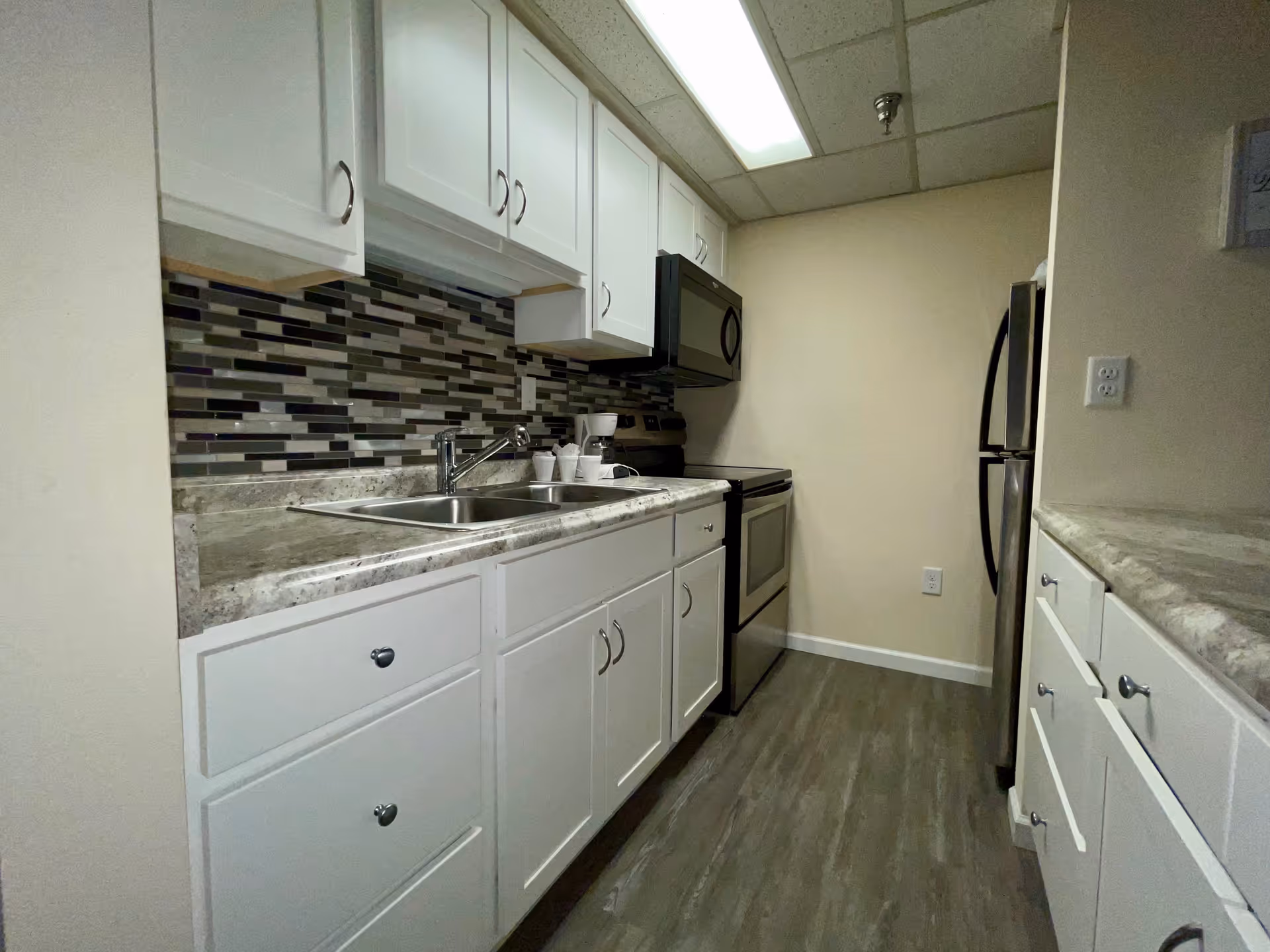Galley kitchen with white cabinets, stainless steel sink and appliances, and a multicolored tile backsplash.