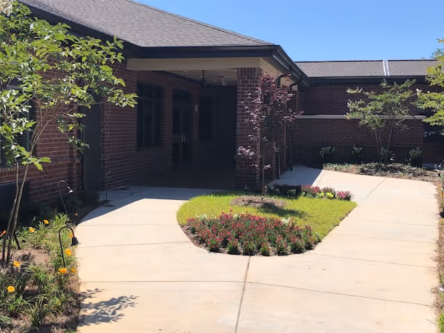 Covered brick building entrance with a sidewalk leading to double doors and a small landscaped courtyard.