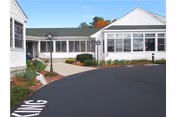 Single-story white nursing home building with a paved driveway and landscaped entrance.