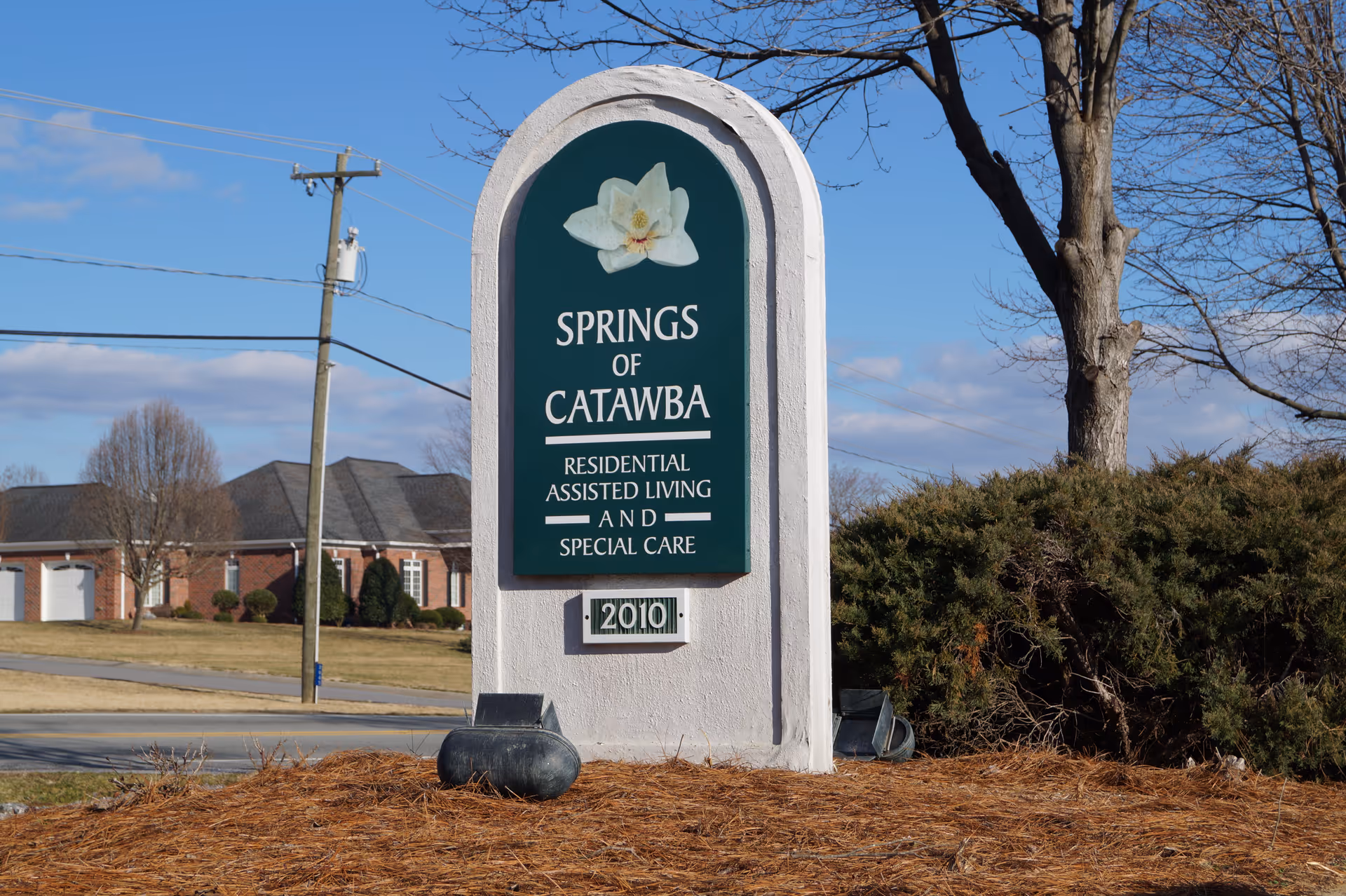 Entrance sign for Springs of Catawba residential assisted living on a landscaped lawn with the facility and trees in the background.