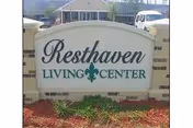 Stone entrance sign that reads "Resthaven Living Center" with mulch and plants in front and a building in the background.