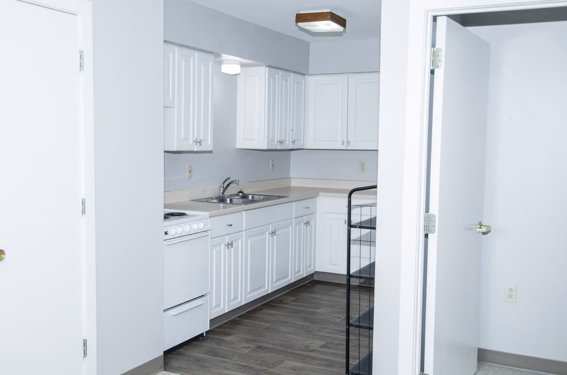 Small kitchen with white cabinets, a sink, stove, and laminate flooring visible through an interior doorway.