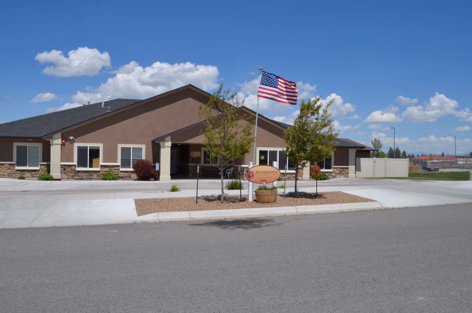 Front view of a single-story Renaissance Senior Care building with an American flag and landscaped entrance under a clear blue sky.
