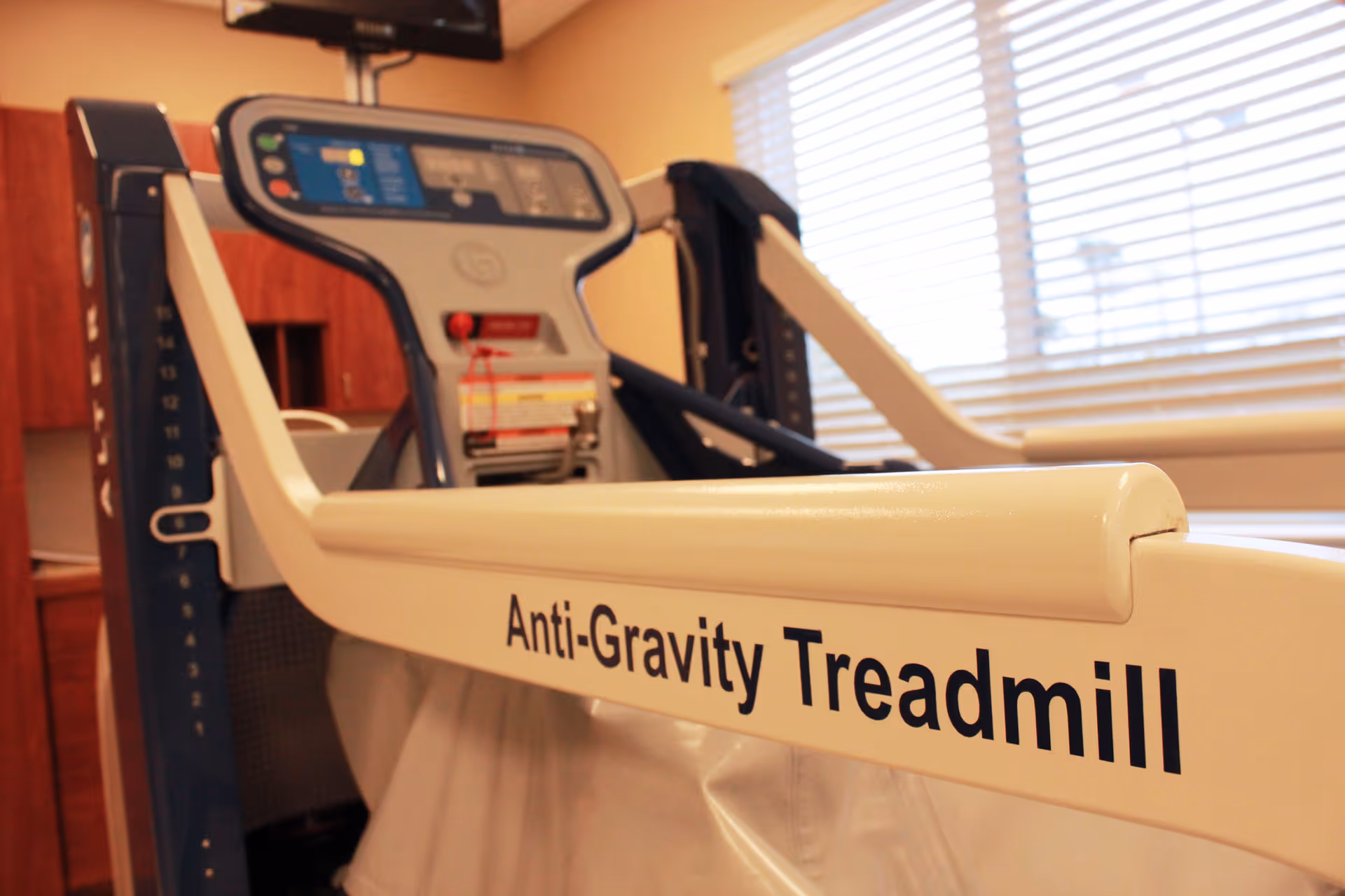 Close-up view of an Anti-Gravity Treadmill in a room with wooden cabinets and a window with blinds.