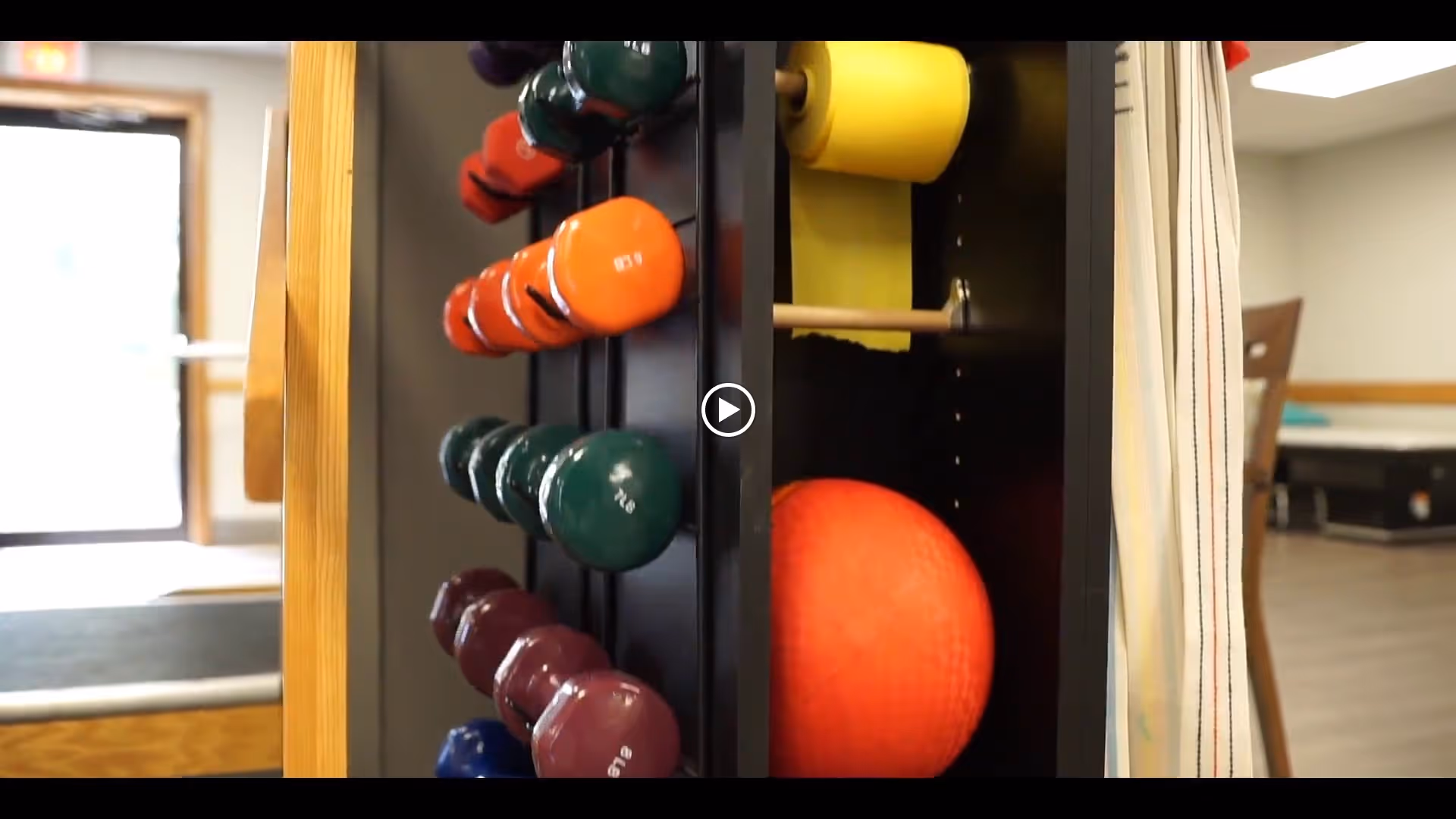 Rack of colorful dumbbells and an orange exercise ball in an indoor fitness/activity room.