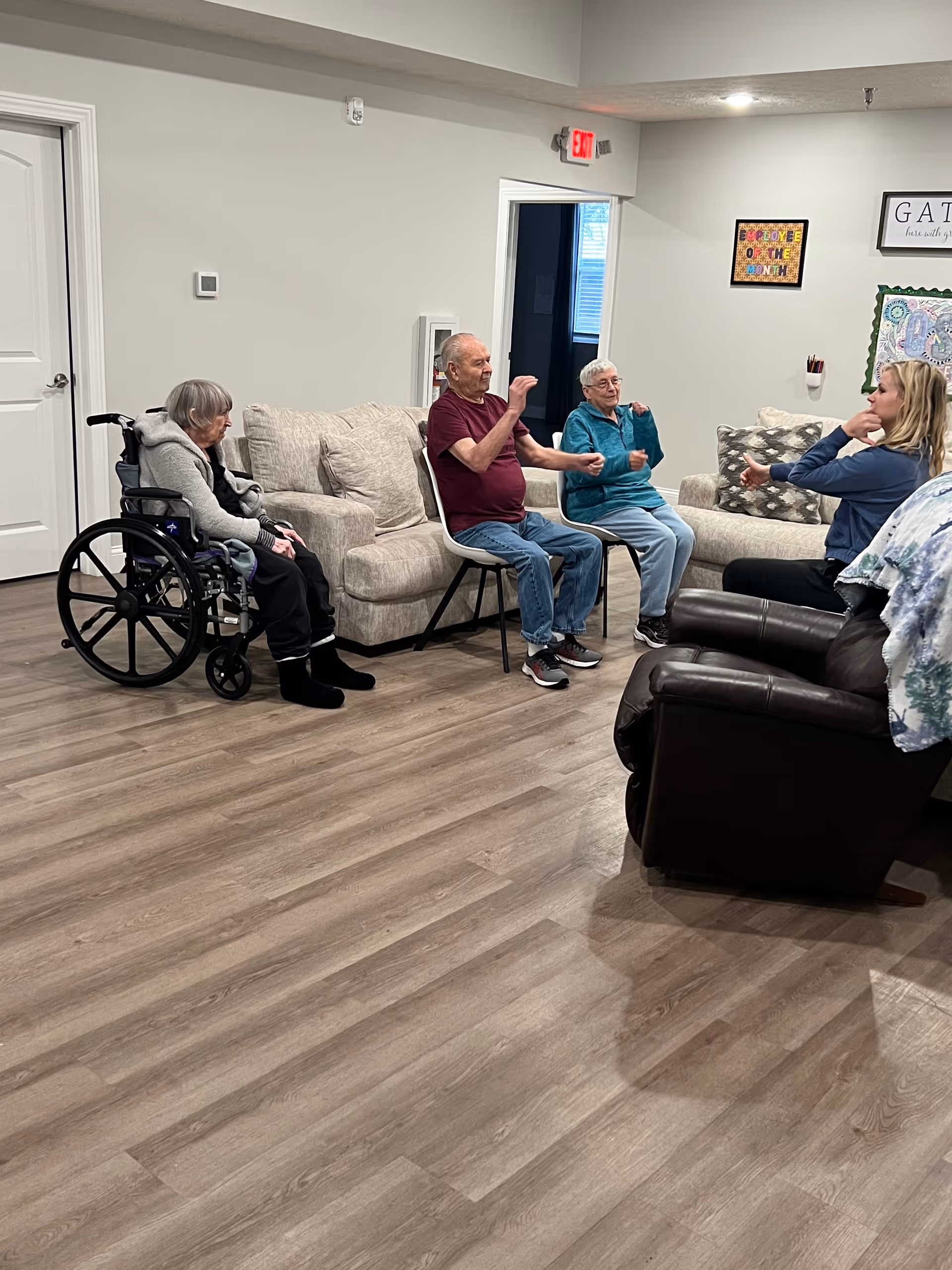 Several seniors seated in a common room participating in a group activity with a staff member.