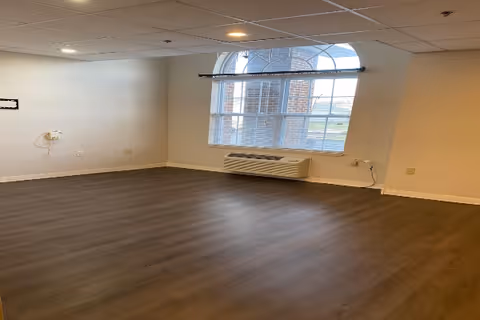 Empty room with wood-look flooring, drop ceiling, a large arched window, and a wall-mounted HVAC unit beneath the window.