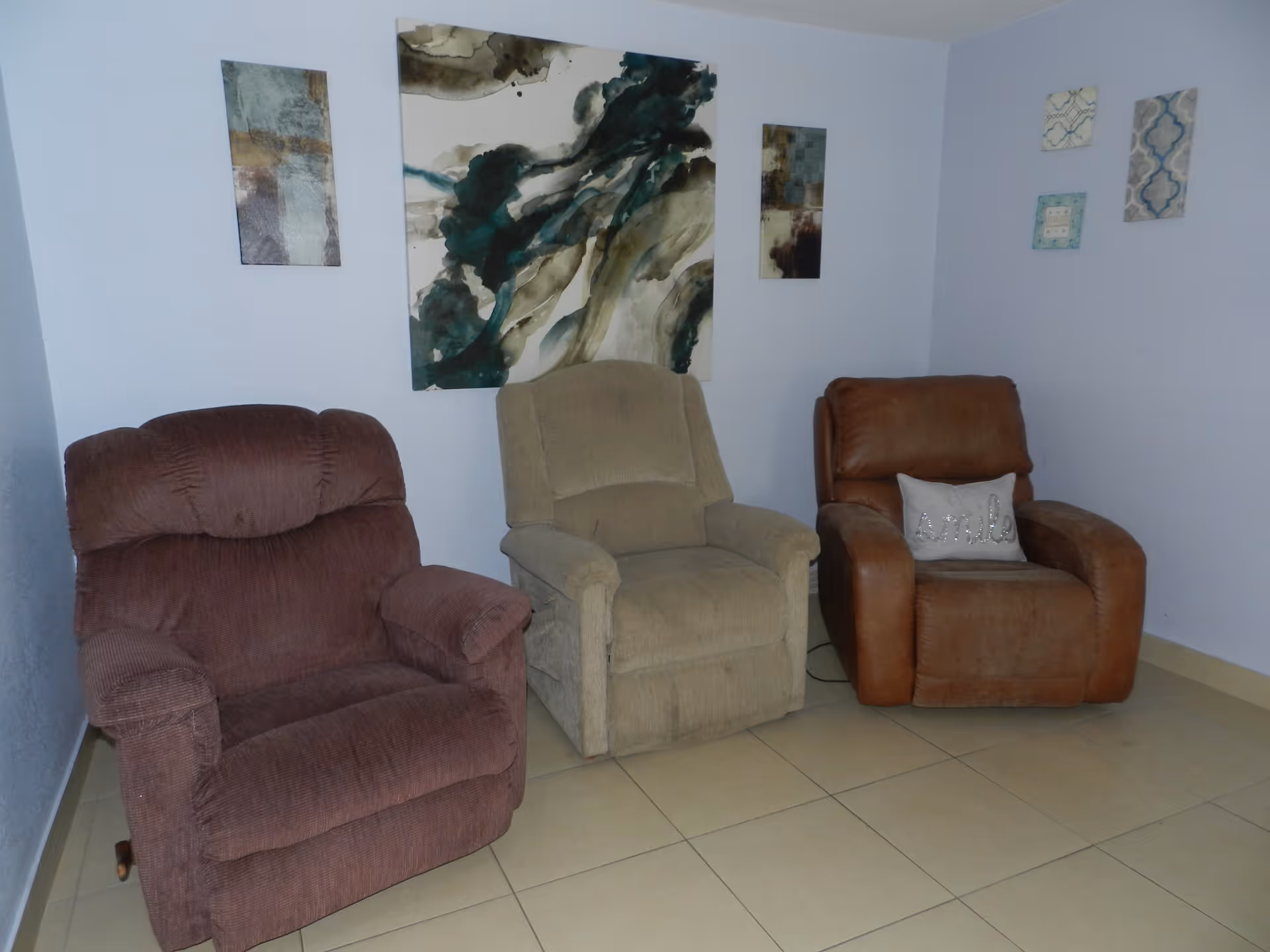 Three upholstered recliner chairs arranged against a light blue wall with decorative wall art above.