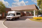 Covered main entrance of a brick senior living facility with a shuttle van parked under the porte-cochère.