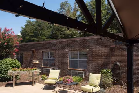 Brick exterior with an outdoor patio, cushioned chairs, and potted plants.