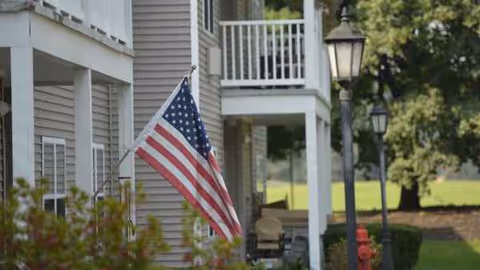 Exterior view of Kingsway Arms Nursing Center with a waving American flag and lampposts.