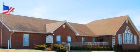 Exterior view of a brick nursing home with a flag and entrance stairs.