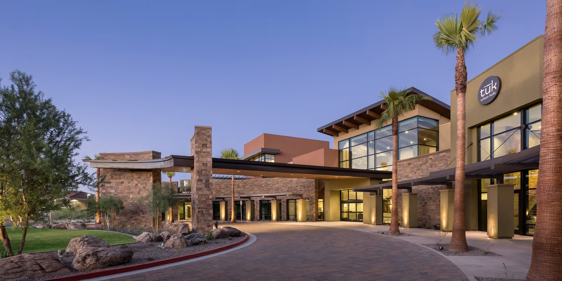 Exterior view of Clearwater Ahwatukee facility at dusk, showing a modern building with large windows, stone and stucco walls, palm trees, and a covered driveway entrance.