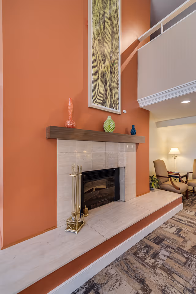 Indoor common area with a tiled fireplace set into an orange wall, decorative vases on the mantel, and seating visible to the right.