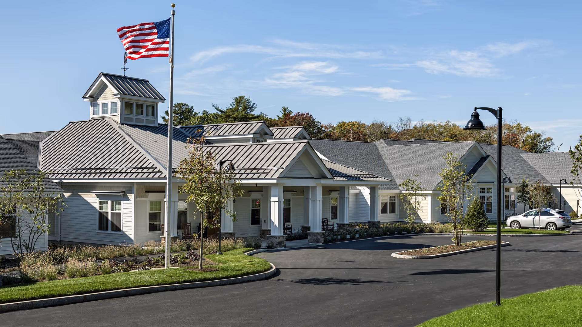 Front entrance of a single-story senior living facility with a covered portico, American flag, and a curved driveway.