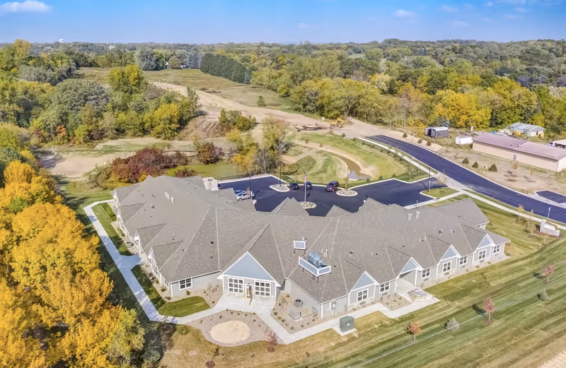 Aerial exterior view of a single-story senior living facility surrounded by lawns, a parking lot, and trees.