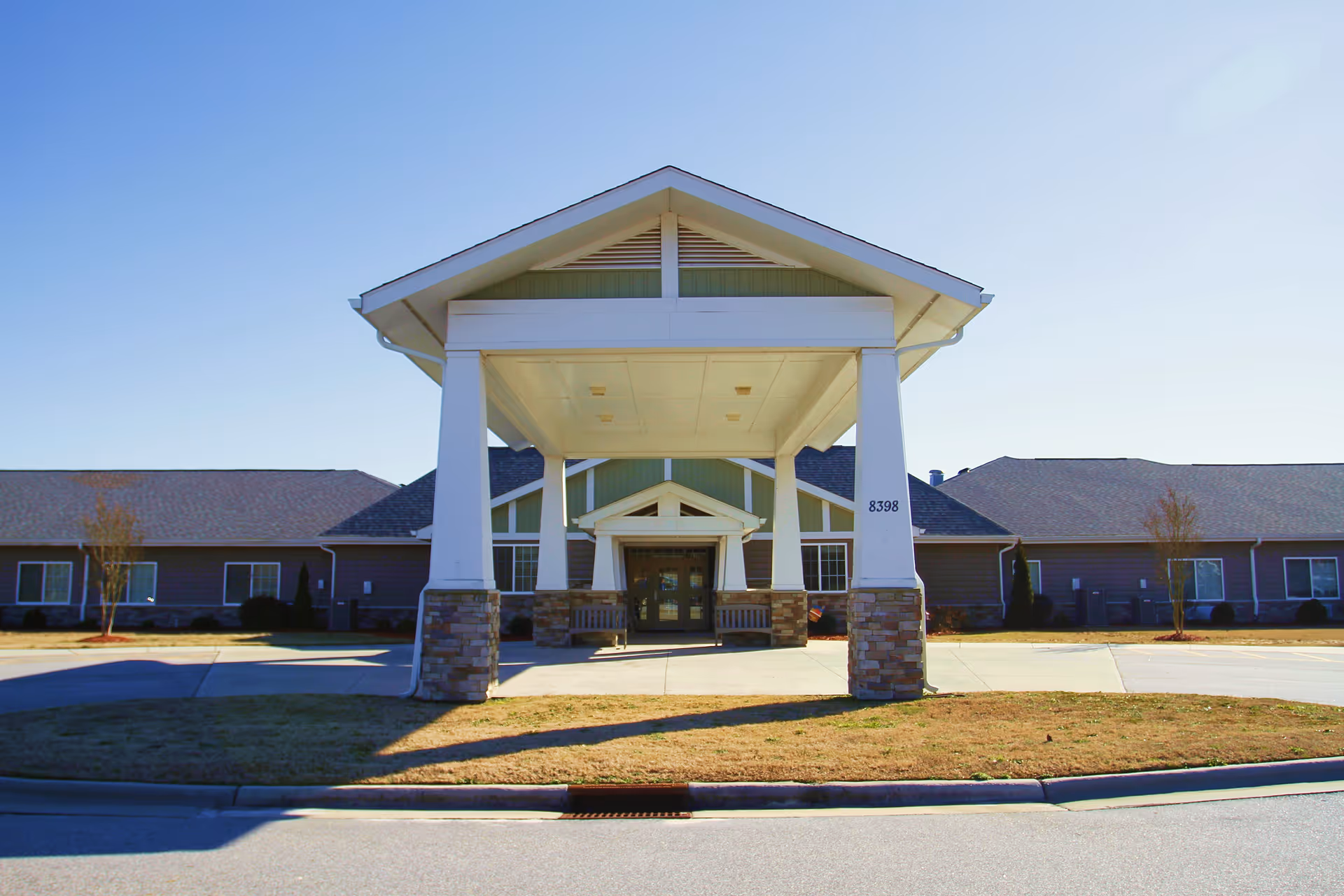 Front entrance of a single-story senior living building featuring a covered porte-cochere supported by white columns with stone bases.