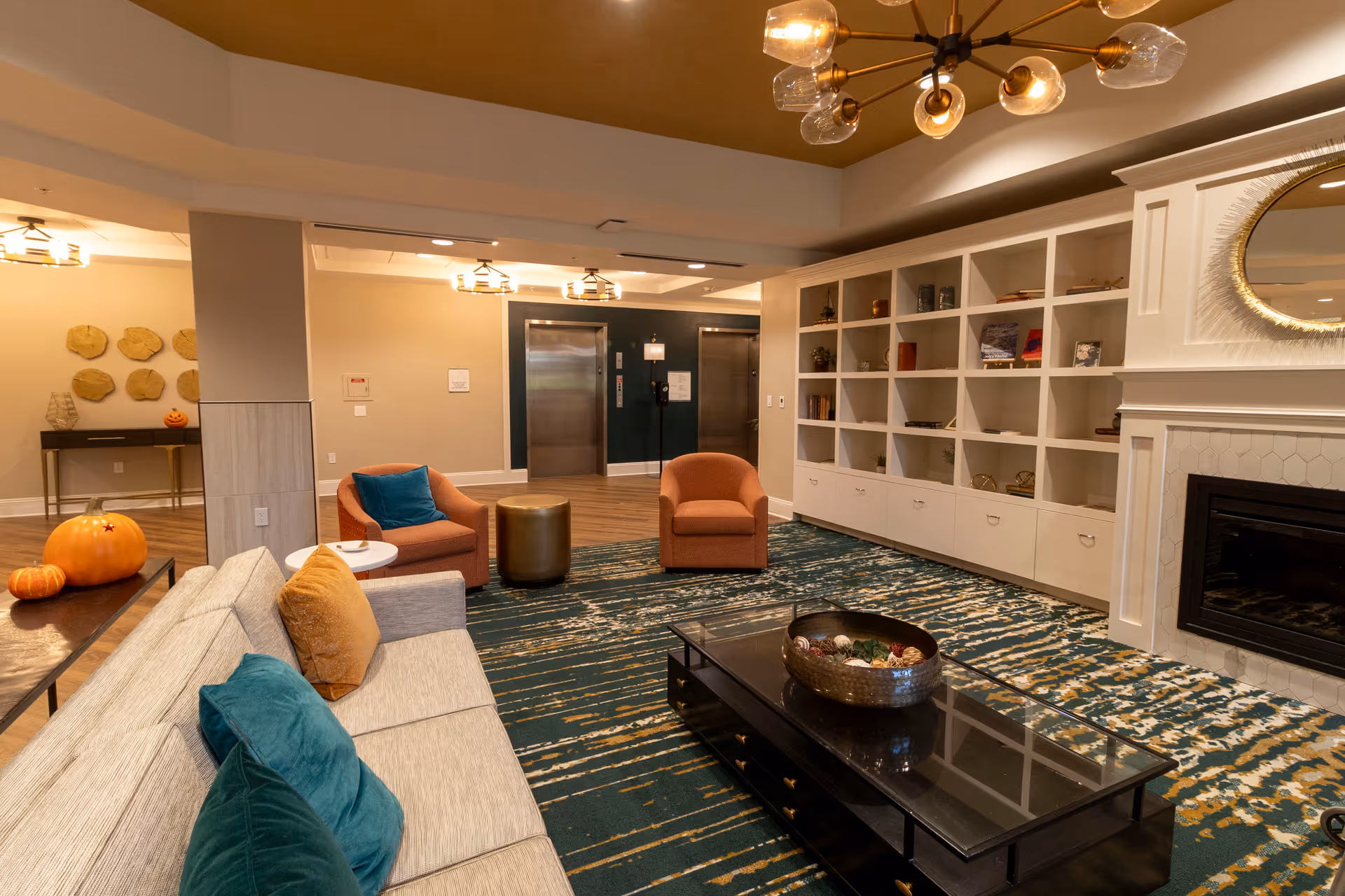 Comfortable communal living room with sofas, armchairs, a coffee table, built-in shelving and a fireplace, decorated for autumn.