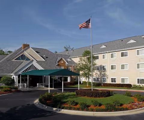 Exterior view of Kauhale Port City senior living facility entrance with flag and landscaping.