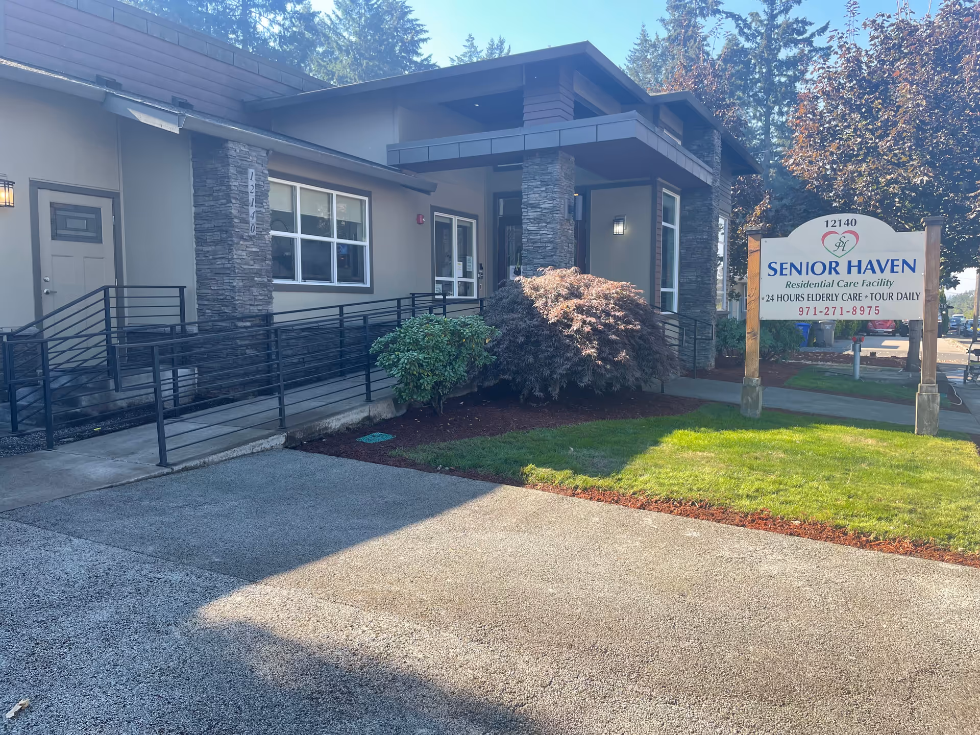 Exterior view of Senior Haven Residential Care Facility showing the entrance with a ramp, stone pillars, windows, and a sign displaying the facility name, address, and contact information.