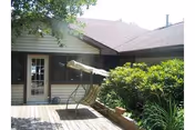 Outdoor patio area of a retirement facility with a wooden deck, a cushioned swing chair, green bushes, and a door leading inside the building.