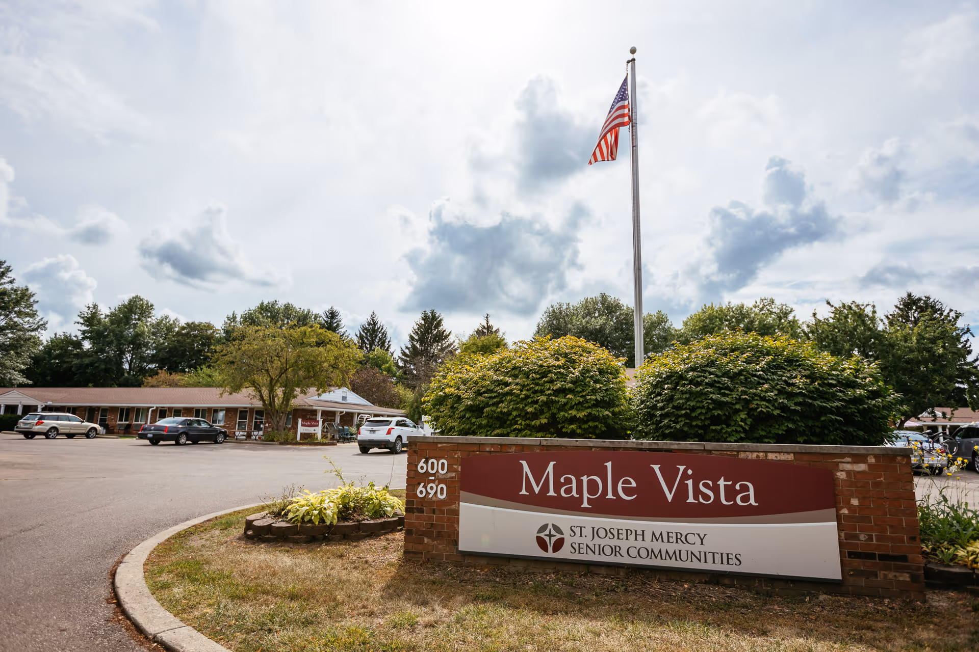 Entrance sign reading "Maple Vista" in front of a single-story senior community building, an American flag, and a parking lot.