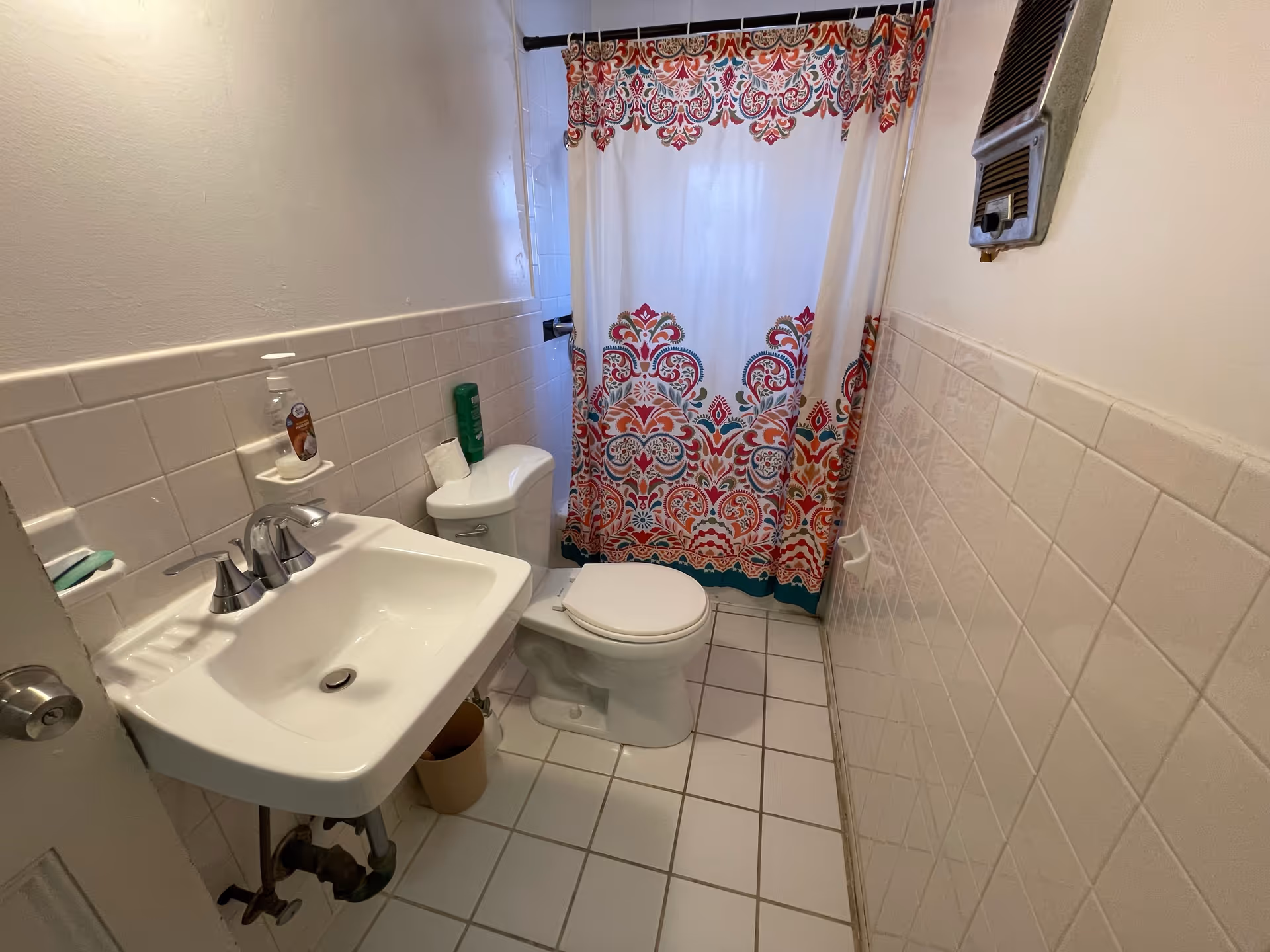 Compact bathroom featuring sink, toilet, and colorful patterned shower curtain.