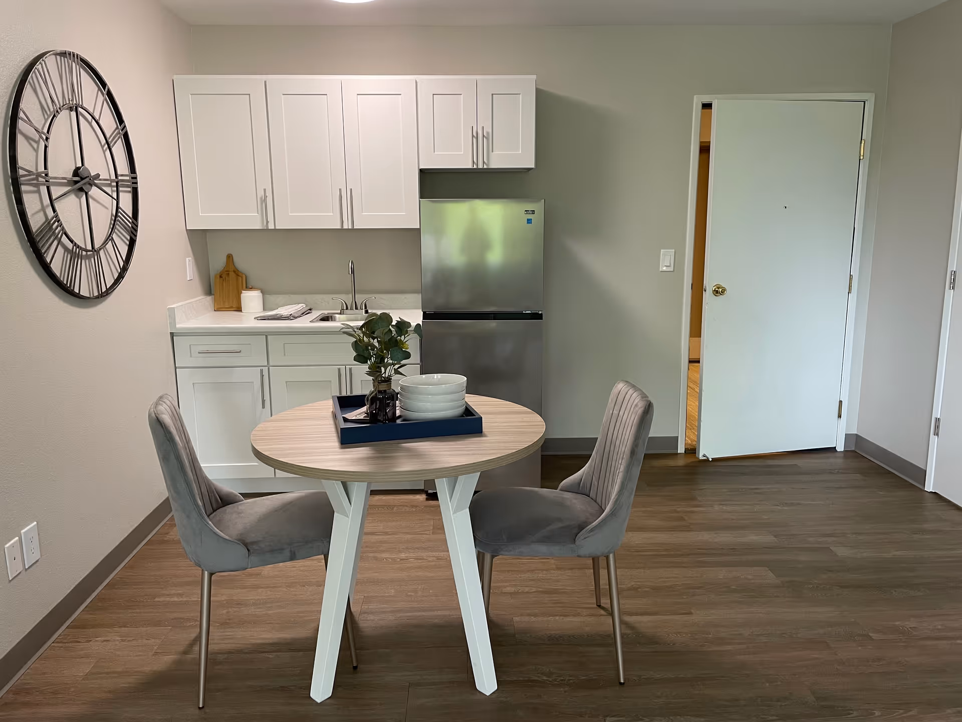 Round dining table with two gray chairs beside a small kitchen area.