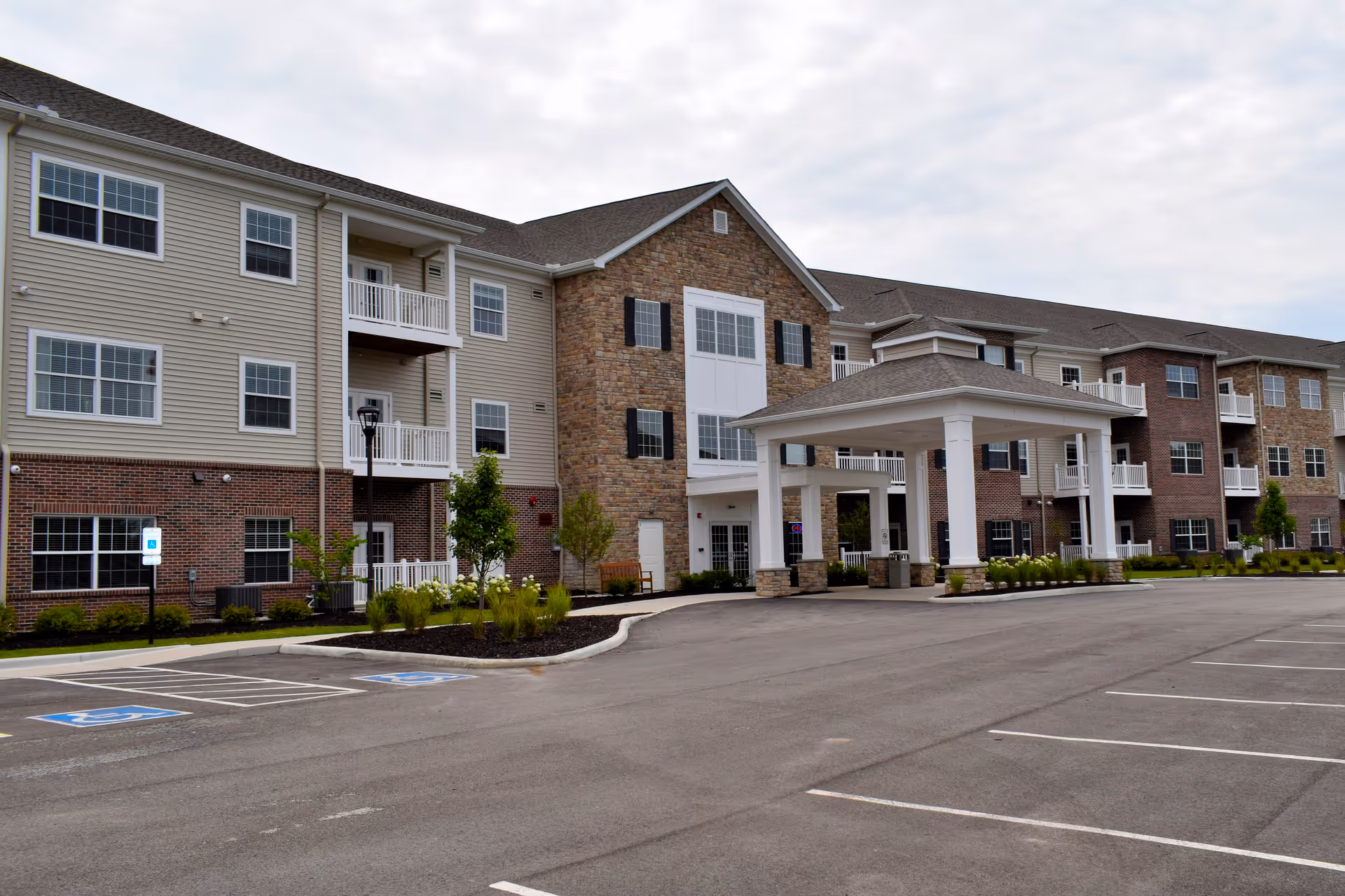 Exterior view of a multi-story senior living facility named Springwood Hudson with a covered entrance, multiple windows, balconies, and a large parking lot with handicap parking spaces.