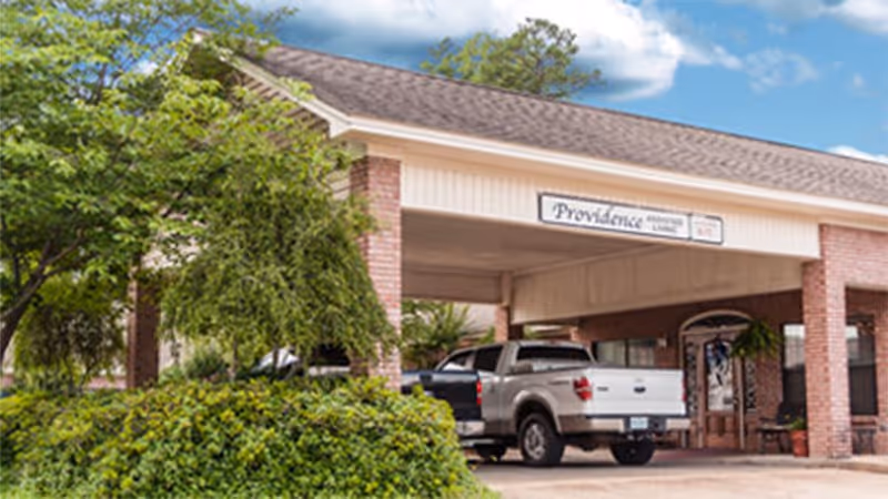 Covered entrance of Providence Assisted Living with a pickup truck parked under the drive-through portico and landscaping in front.