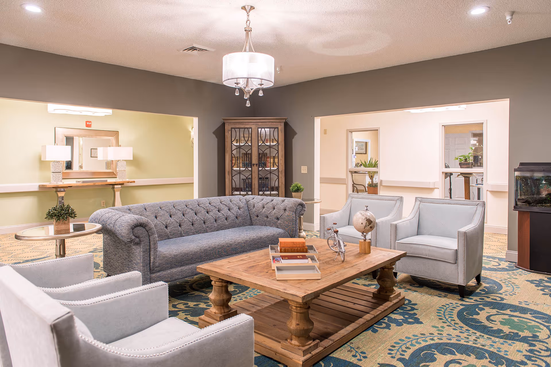 Bright living room lounge with a tufted gray sofa, blue chairs, and a wooden coffee table.