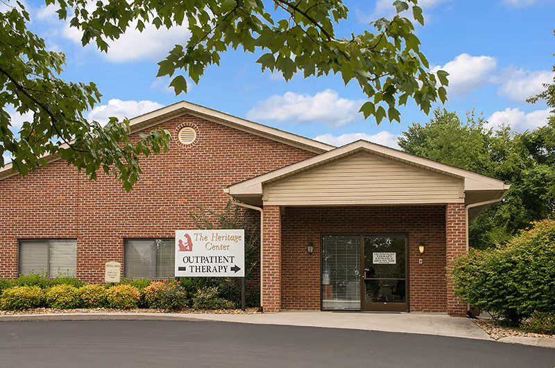 Brick single-story building entrance for The Heritage Center with a sign directing to outpatient therapy.