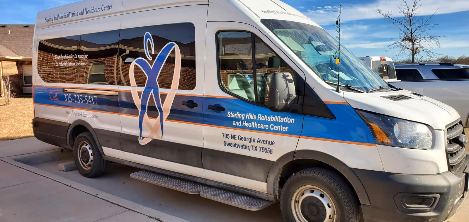 Branded Sterling Hills Rehabilitation and Healthcare Center shuttle van parked outside a building.