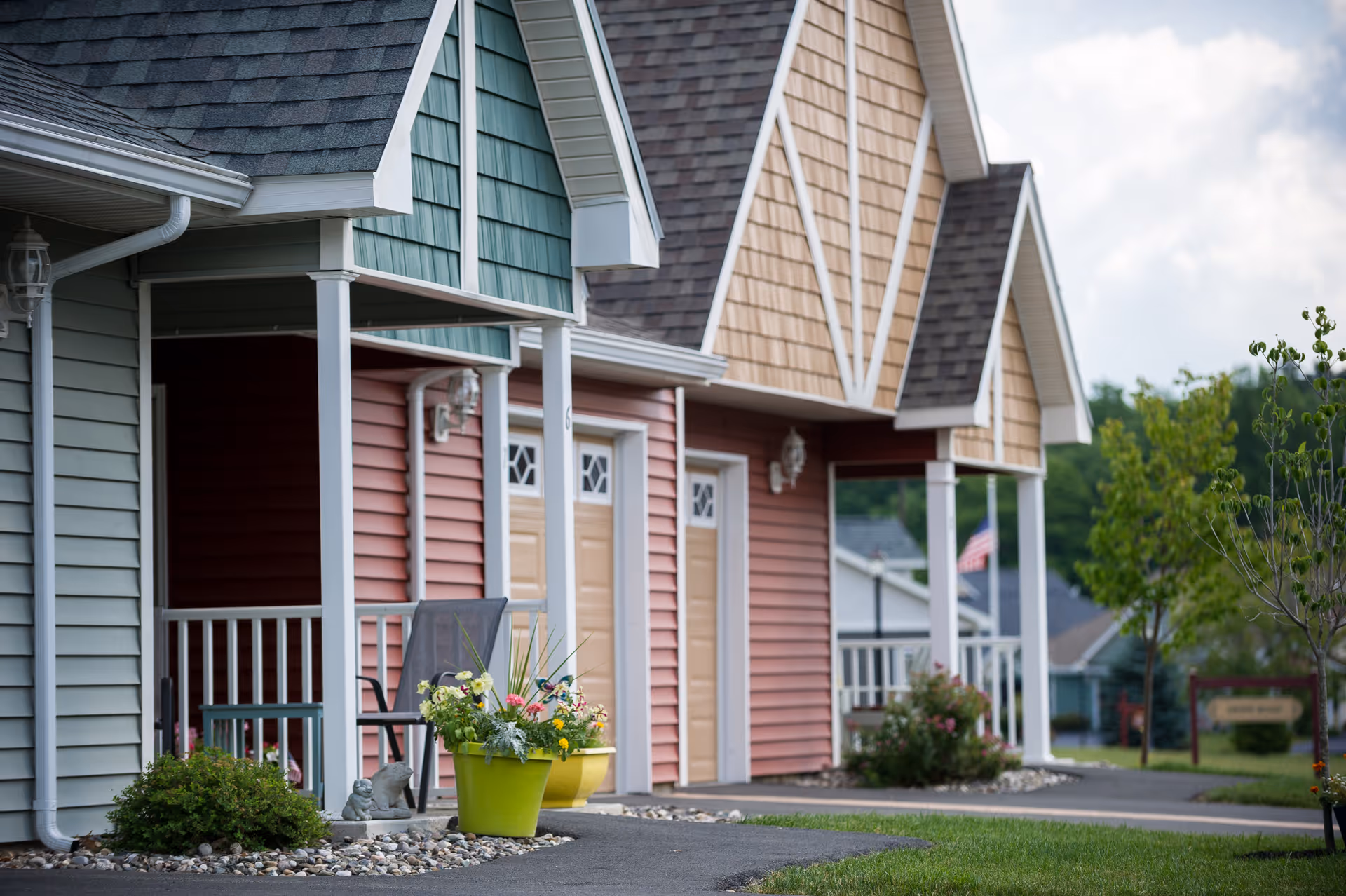 Row of colorful cottage-style units with small porches, potted flowers, and driveways at a senior living community.