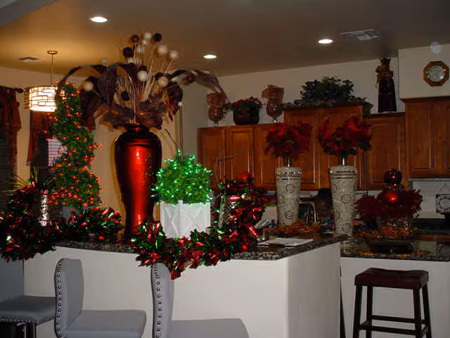 Decorated kitchen with a countertop bar and stools, wooden cabinets, and festive red and green holiday arrangements including a large red vase.