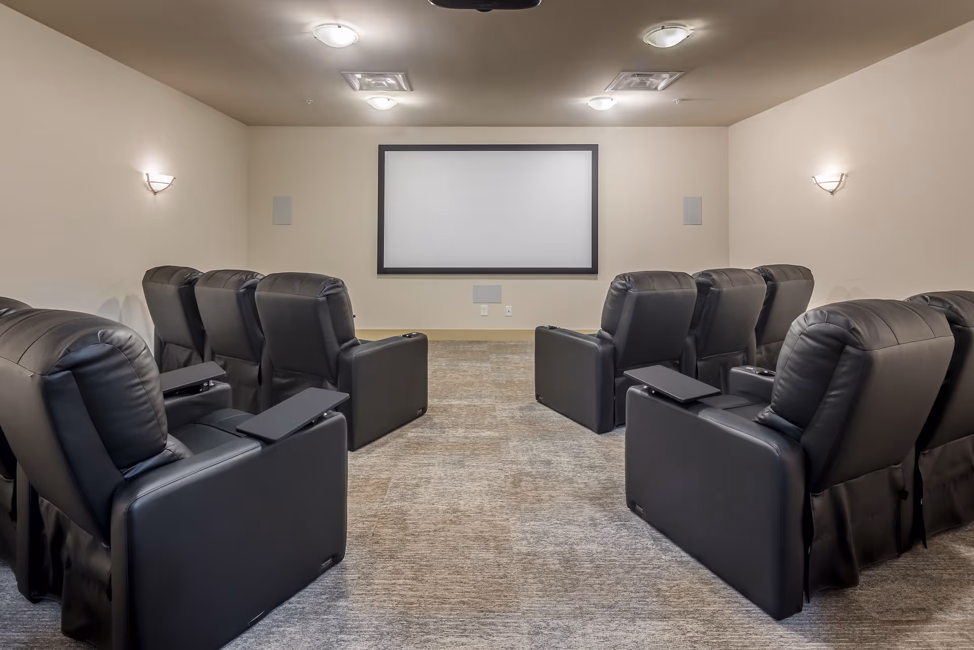Small screening room with two rows of black leather recliners facing a blank projection screen.